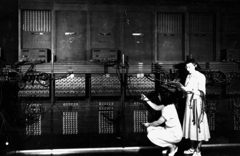 Deux techniciennes reconfigurent l'ENIAC en manipulant câbles et interrupteurs.